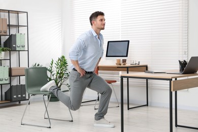 Photo of Handsome man exercising with chair in office