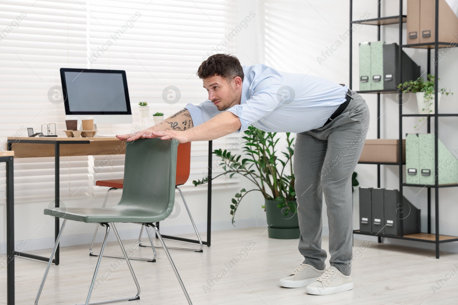 Handsome man exercising with chair in office Photo of Handsome man exercising with chair in office