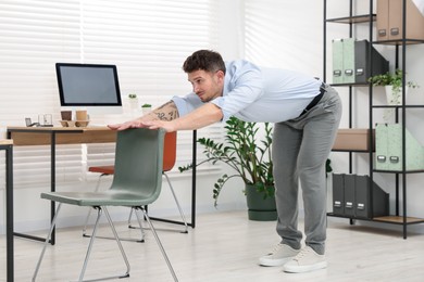 Photo of Handsome man exercising with chair in office