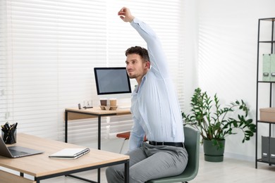 Photo of Handsome man stretching on chair in office