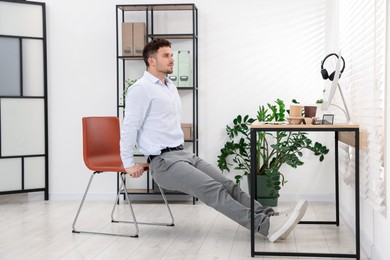 Photo of Handsome man exercising with chair in office