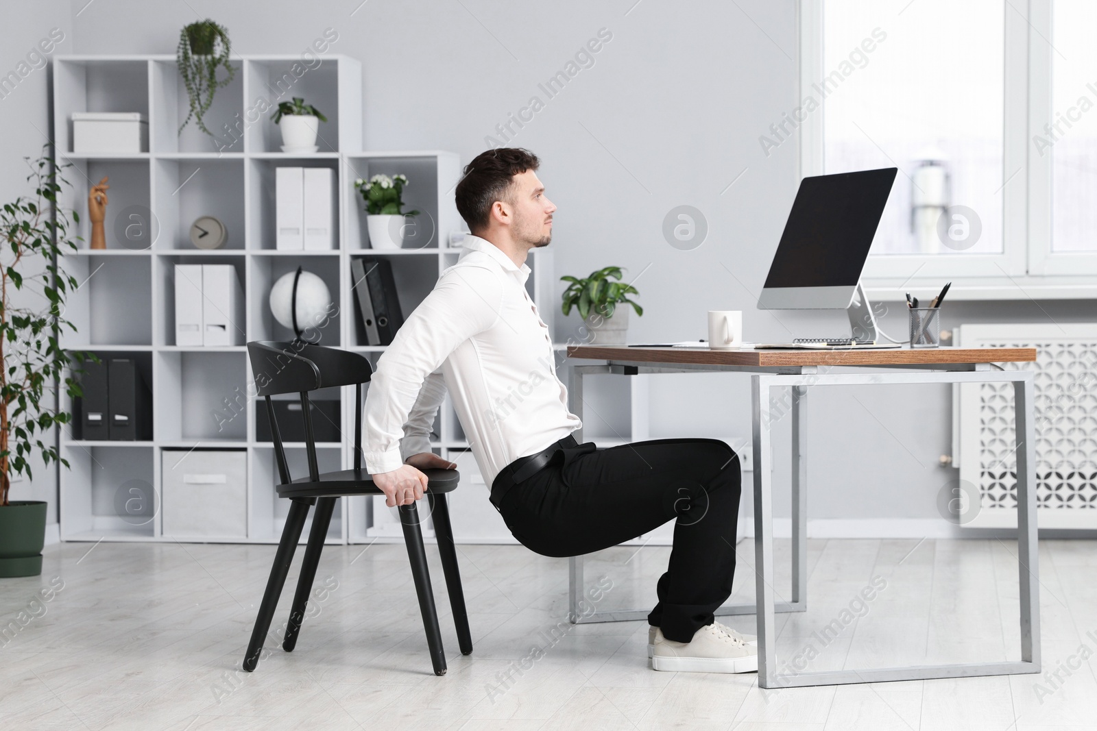 Handsome man exercising with chair in office Photo of Handsome man exercising with chair in office