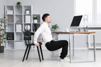 Photo of Handsome man exercising with chair in office