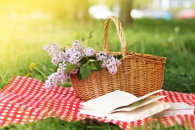 Photo of Books, blanket and wicker basket with lilac flowers on green grass outdoors