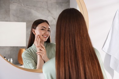 Photo of Beautiful woman looking at herself in mirror indoors