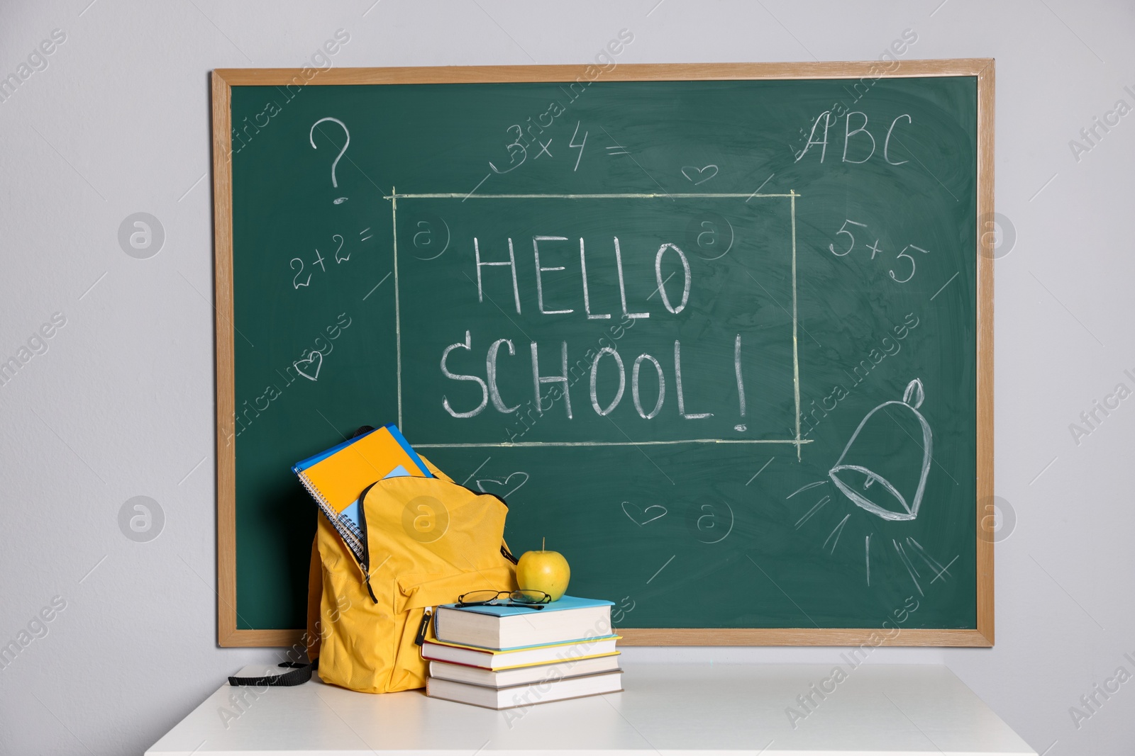 Phrase Hello School with exclamation mark on blackboard, backpack and different stationery indoors Photo of Phrase Hello School with exclamation mark on blackboard, backpack and different stationery indoors