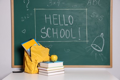 Photo of Phrase Hello School with exclamation mark on blackboard, backpack and different stationery indoors