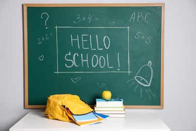 Photo of Phrase Hello School with exclamation mark on blackboard, backpack and different stationery indoors