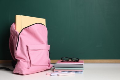 Photo of Blank green chalkboard, different stationery, backpack and glasses, space for text