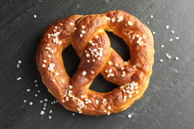 Photo of Tasty pretzel with salt on black table, top view