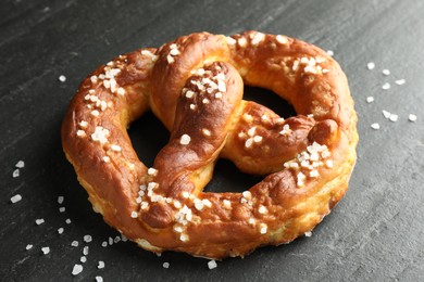 Photo of Tasty pretzel with salt on black table, closeup