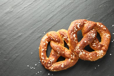Photo of Tasty pretzels with salt on black table, flat lay. Space for text