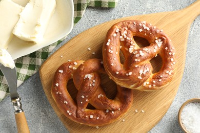 Photo of Tasty pretzels with salt and butter on light grey table, flat lay
