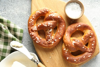 Photo of Tasty pretzels with salt and butter on light grey table, flat lay