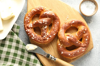 Photo of Tasty pretzels with salt and butter on light grey table, flat lay