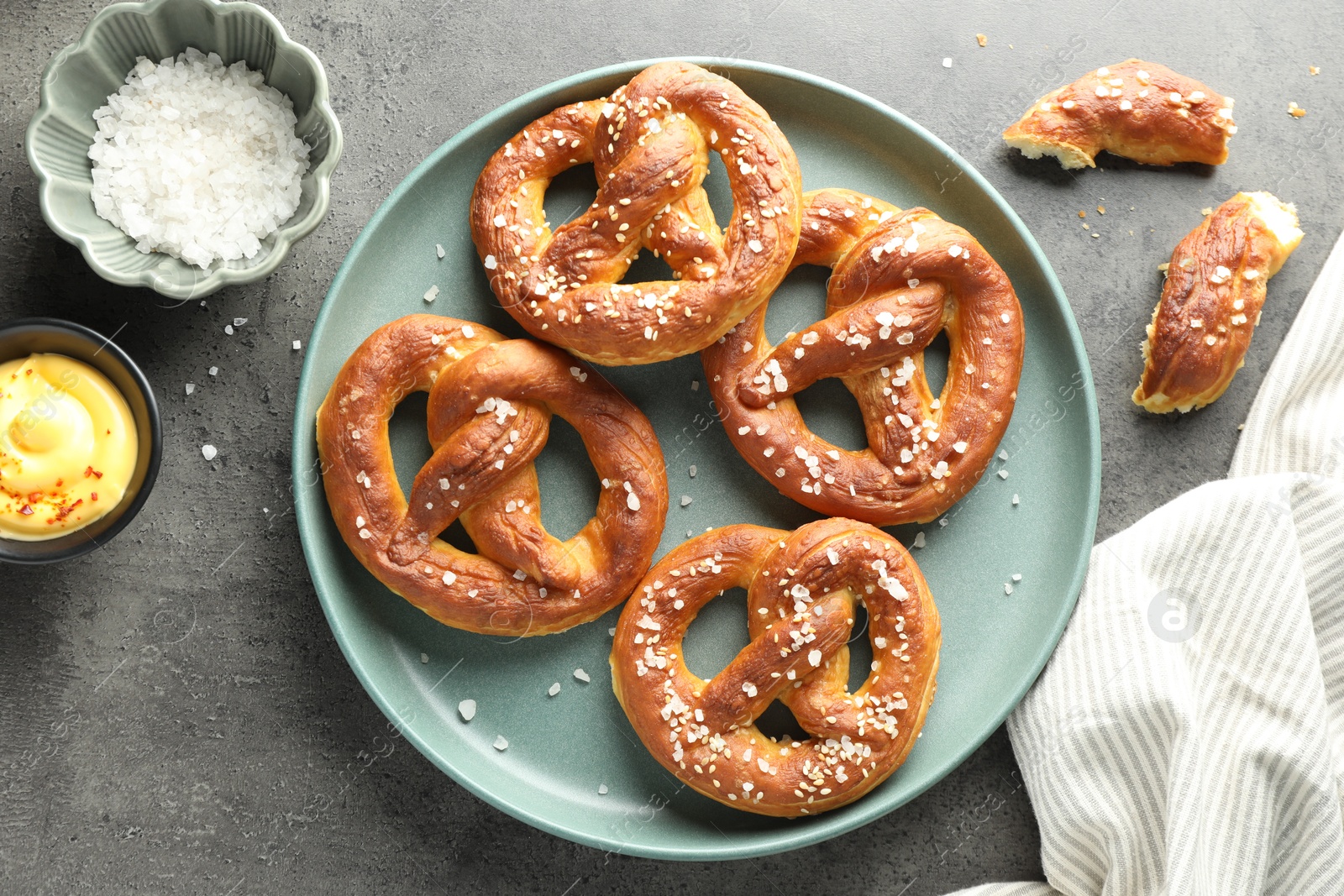 Tasty pretzels with salt and sauce on grey table, flat lay Photo of Tasty pretzels with salt and sauce on grey table, flat lay