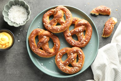 Photo of Tasty pretzels with salt and sauce on grey table, flat lay