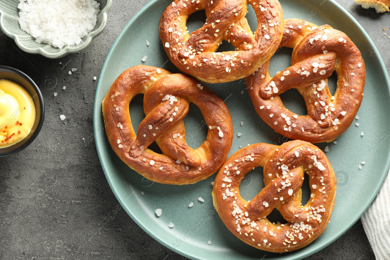 Tasty pretzels with salt and sauce on grey table, flat lay Photo of Tasty pretzels with salt and sauce on grey table, flat lay