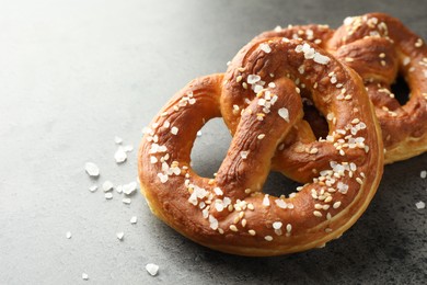Photo of Tasty pretzels with salt on grey table, closeup. Space for text