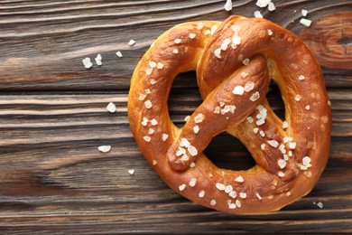 Photo of Tasty pretzel with salt on wooden table, top view. Space for text