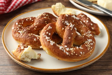 Photo of Tasty pretzels with salt and butter on wooden table, closeup