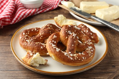 Photo of Tasty pretzels with salt and butter on wooden table, closeup