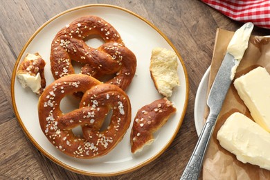 Photo of Tasty pretzels with salt and butter on wooden table, flat lay
