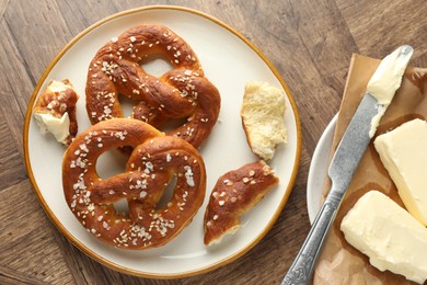 Photo of Tasty pretzels with salt and butter on wooden table, flat lay