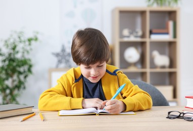 Photo of Cute little boy doing homework at table indoors