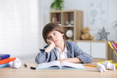 Photo of Tired little boy doing homework at table indoors