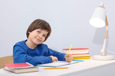 Photo of Cute little boy doing homework at desk indoors