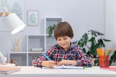 Photo of Cute little boy doing homework at table indoors