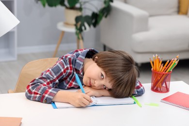 Photo of Cute little boy doing homework at table indoors