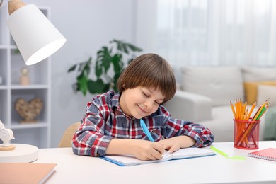 Photo of Cute little boy doing homework at table indoors