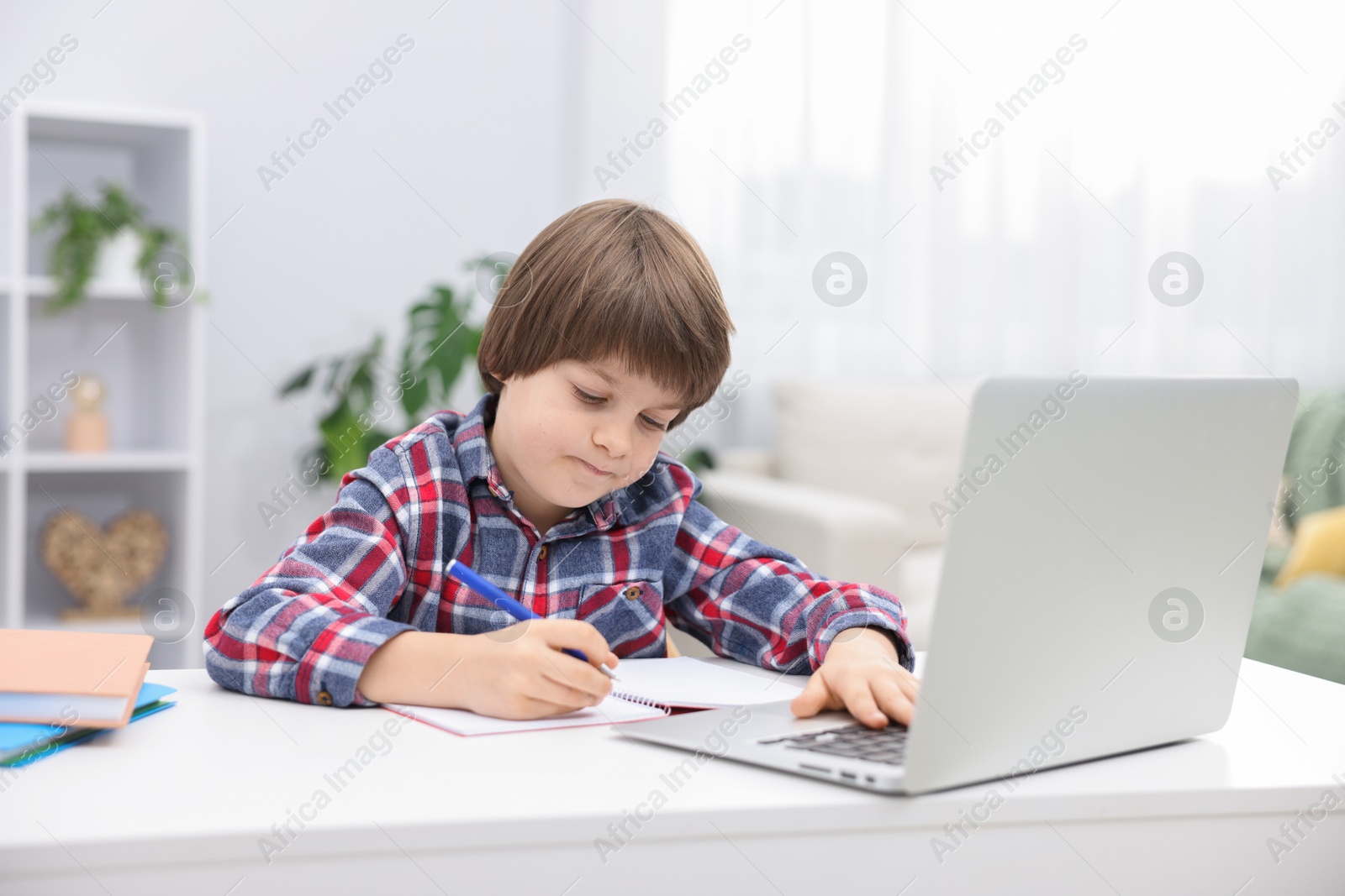 Cute little boy doing homework with laptop at desk indoors Photo of Cute little boy doing homework with laptop at desk indoors