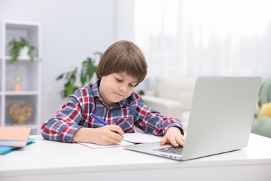 Photo of Cute little boy doing homework with laptop at desk indoors