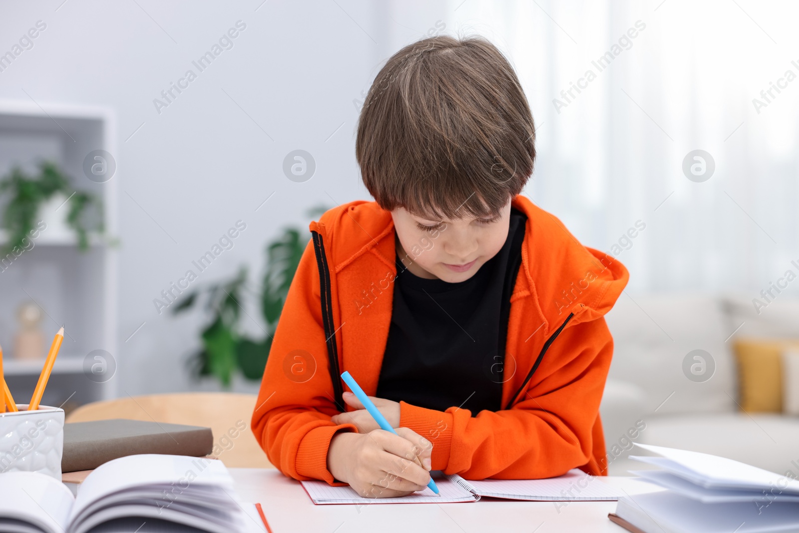 Cute little boy doing homework at desk indoors Photo of Cute little boy doing homework at desk indoors