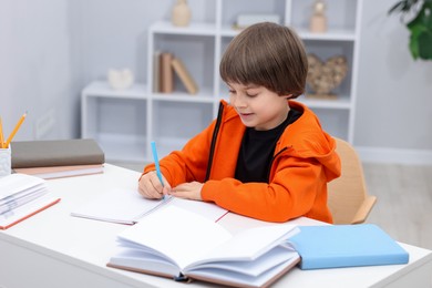 Photo of Cute little boy doing homework at desk indoors