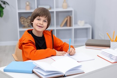 Photo of Cute little boy doing homework at desk indoors