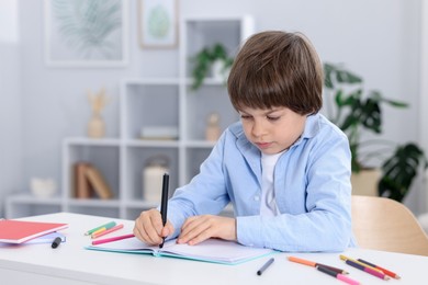 Photo of Cute little boy doing homework at table indoors