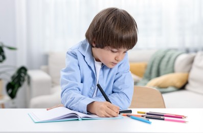 Photo of Cute little boy doing homework at table indoors