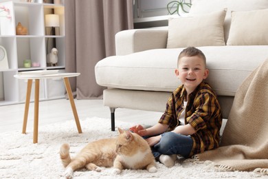 Photo of Little boy with his cute ginger cat at home, space for text