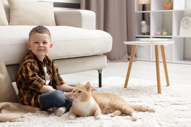 Photo of Little boy with his cute ginger cat at home, space for text