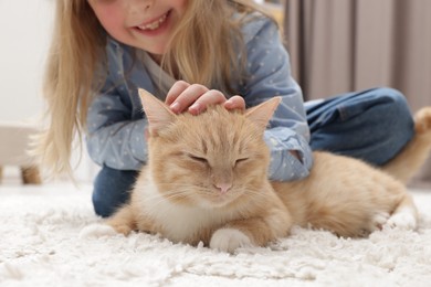 Photo of Little girl with her cute ginger cat at home, closeup