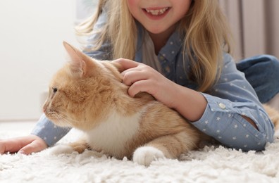 Photo of Little girl with her cute ginger cat at home, closeup