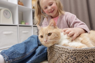 Photo of Little girl with her cute ginger cat at home, selective focus