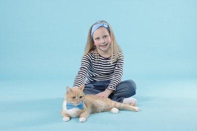 Photo of Little girl with her cute ginger cat on light blue background
