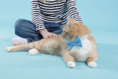 Photo of Little girl with her cute ginger cat on light blue background, closeup
