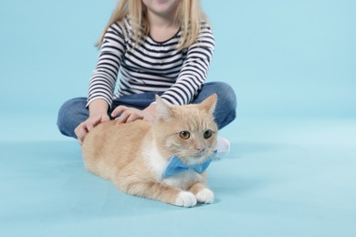 Photo of Little girl with her cute ginger cat on light blue background, closeup