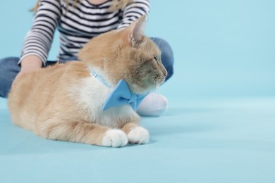 Photo of Little girl with her cute ginger cat on light blue background, closeup. Space for text